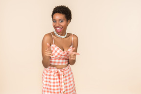 Young black short-haired woman in a checkered top and a skirt, posing against a plain peachy background