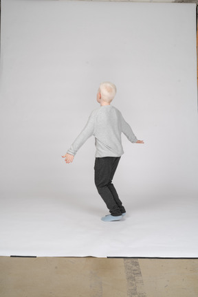Side view of a little boy standing with knees bent and arms spread