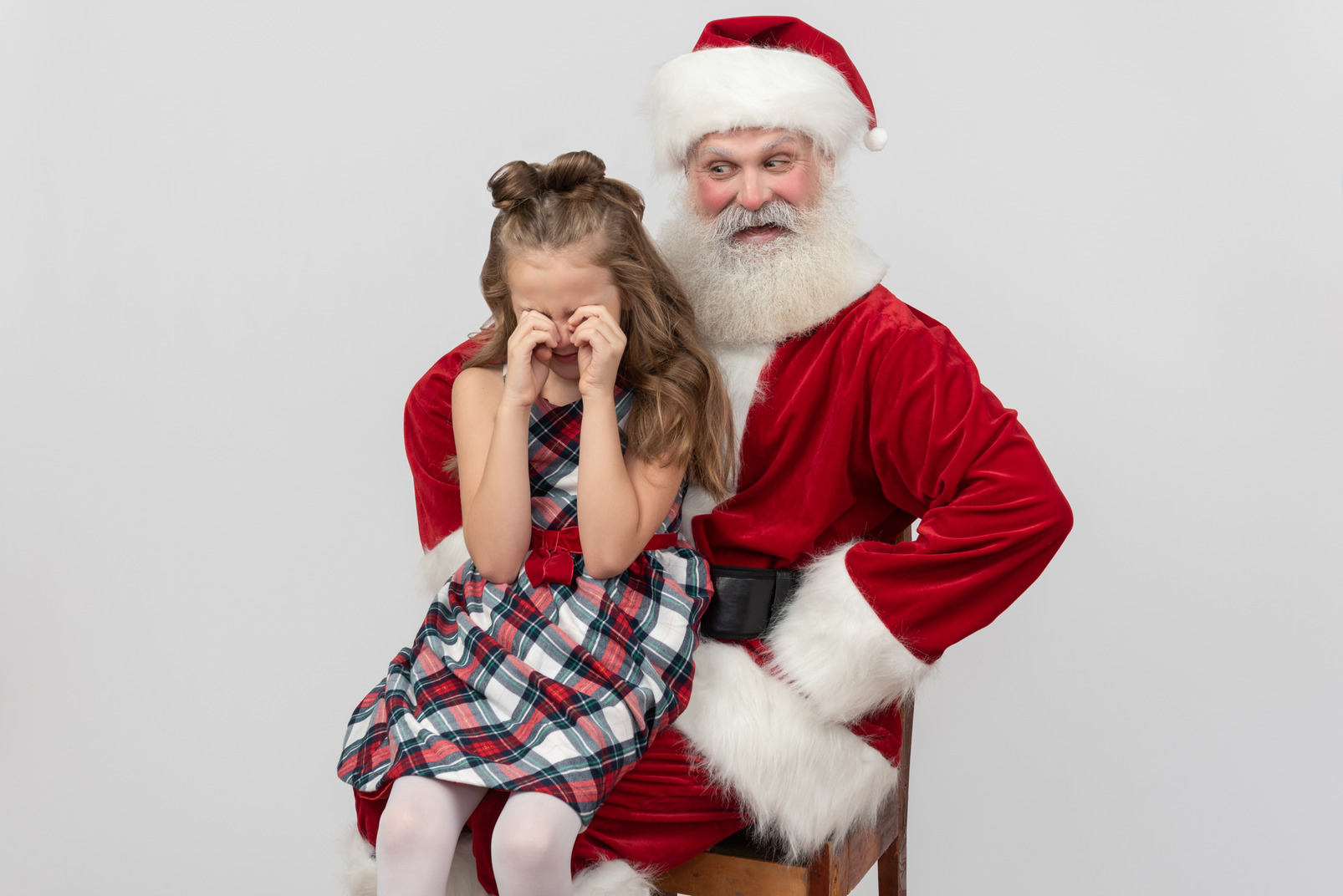 Kid girl sitting on santa's knees and crying