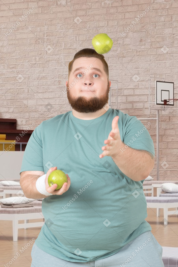A fat man juggling apples in a room with beds