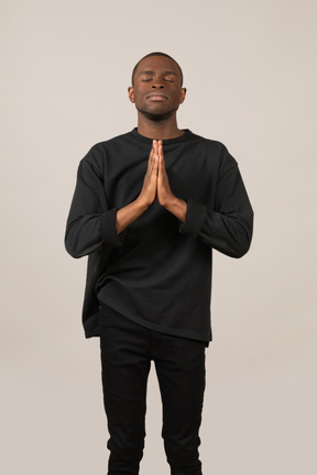 Junger mann betet mit geschlossenen augen und zusammengehaltenen händen
