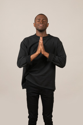 Young man praying with eyes closed and hands held together