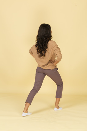 Three-quarter back view of a squatting dark-skinned young female making a lunge