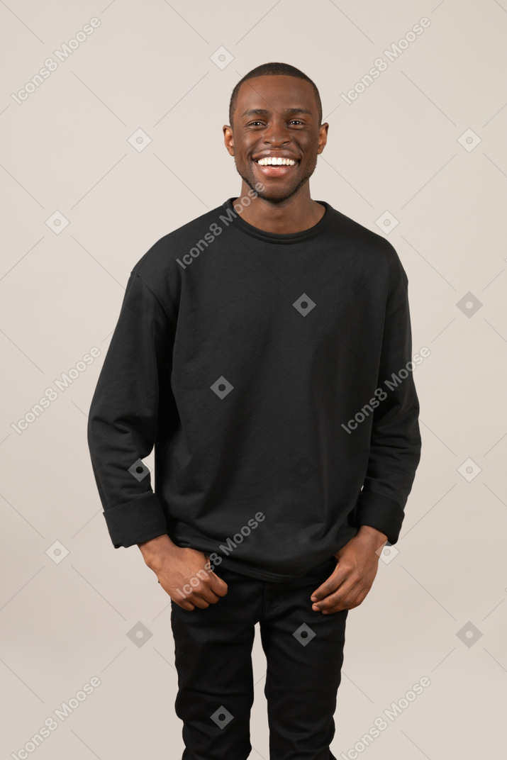 Молодой человек улыбается, засунув руки в карманы