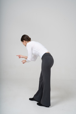 Вид сбоку женщины в черных брюках и белой блузке, наклоняющейся вниз