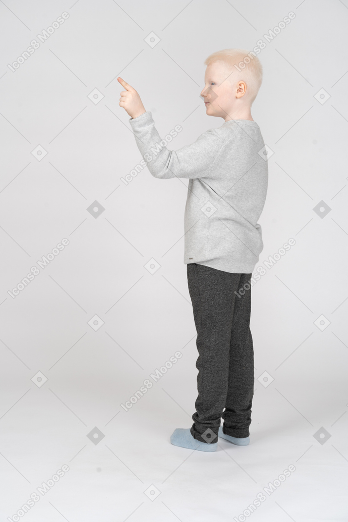 Маленький мальчик стоит и показывает указательным пальцем