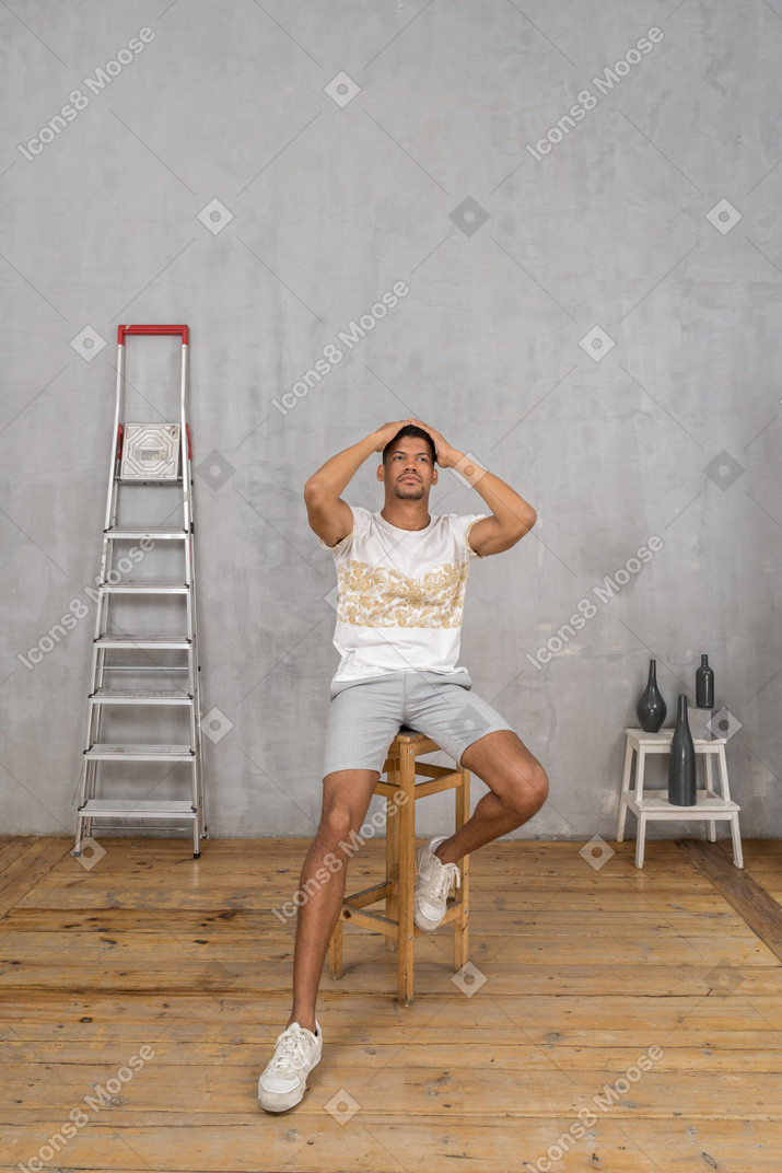 Front view of man sitting on stool with hands on his head