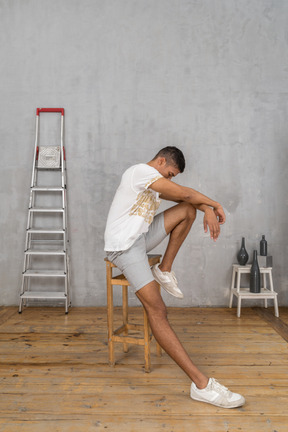 Pensive young man sitting on stool and looking down