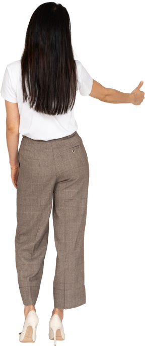 Vista posteriore di una giovane donna in calzoni e maglietta che mostra il pollice in su