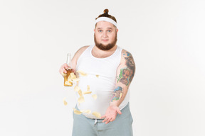 A fat man in sportswear holding a bottle of beer and throwing up chips