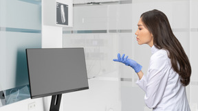 A woman in a white lab coat is looking at a monitor