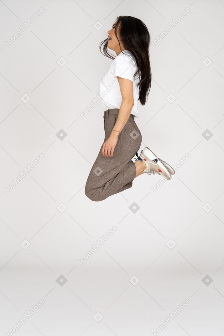 Vista frontale di una giovane donna che salta in calzoni e t-shirt piegare le ginocchia