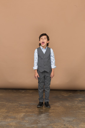 Vista frontale di un ragazzo carino in abito grigio che fa smorfie e mostra la lingua