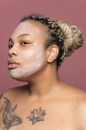 Frau mit einer kosmetischen maske auf ihrem gesicht, das transparenten spiegel betrachtet