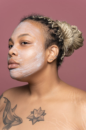 Femme avec un masque cosmétique sur son visage regardant miroir transparent