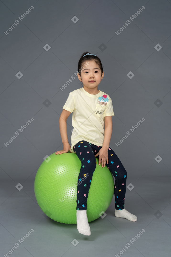 Kleines mädchen, das auf einem grünen fitball sitzt