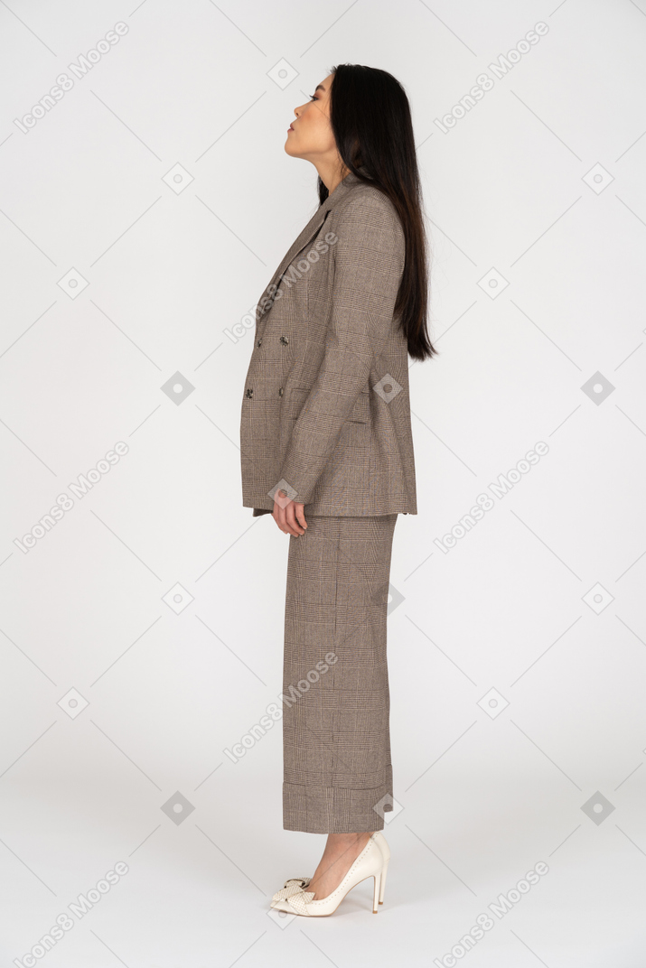 Vista lateral de una señorita en traje marrón levantando la cabeza