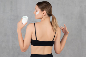 Young woman holding a face cream and looking over her shoulder