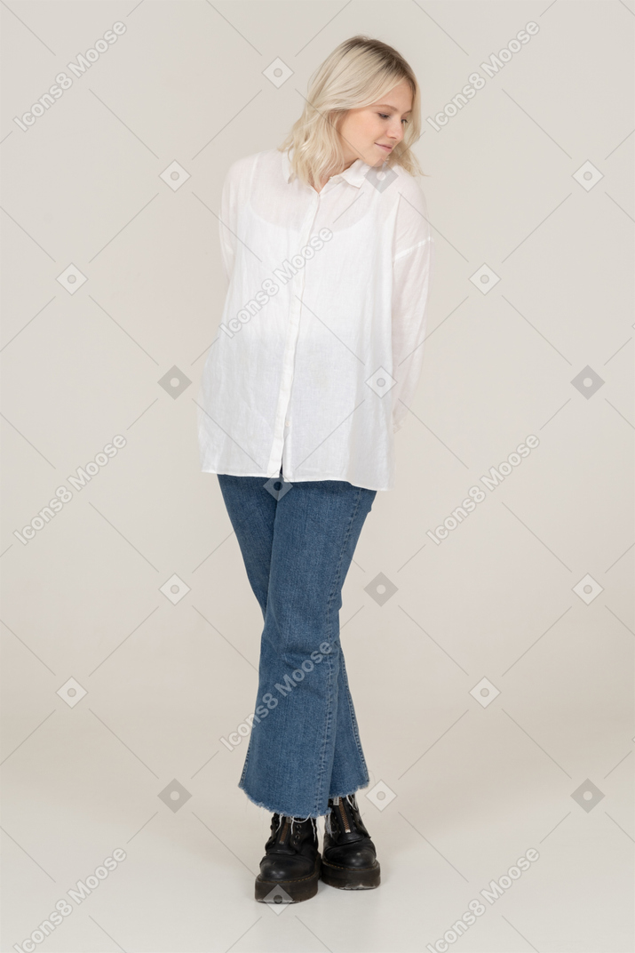 Front view of a shy blonde female in casual clothes crossing legs and looking down