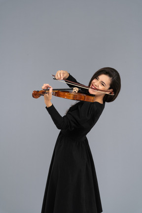 Close-up de uma jovem alegre de vestido preto tocando violino