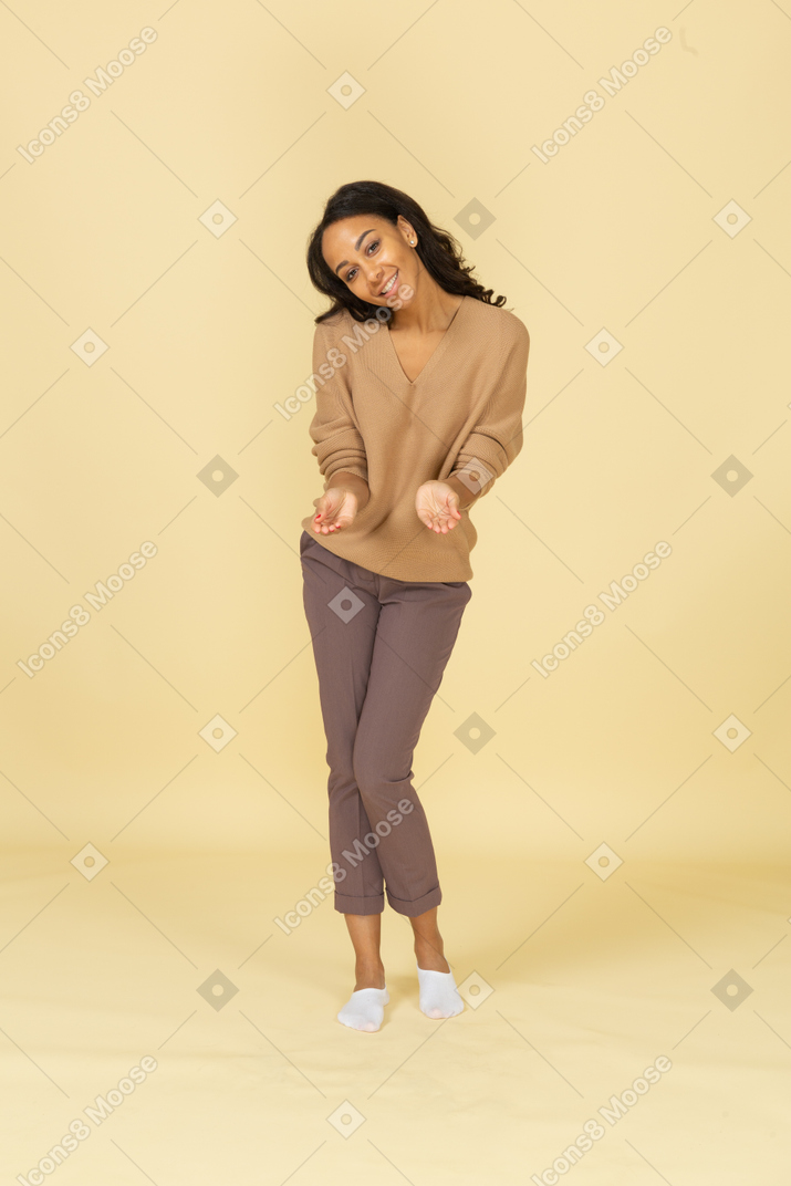 Vista frontal de una mujer joven sonriente de piel oscura extendiendo sus manos