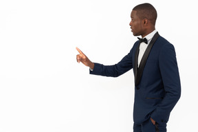 Good-looking young business man standing in profile and pointing with his hand