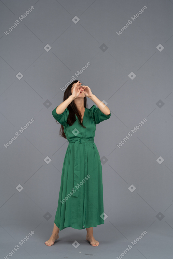 Front view of a young lady in green dress playing flute while raising hands