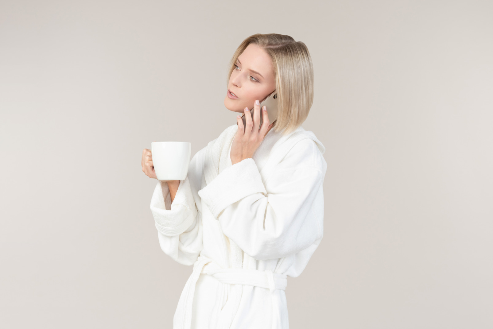 Young woman in bathrobe holding mug and talking on the phone