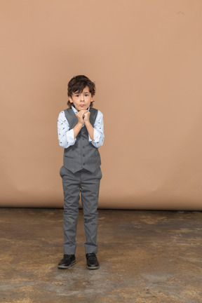 Front view of a cute boy in grey suit making praying gesture