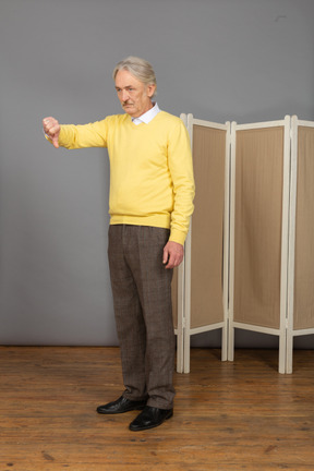 Vista de três quartos de um homem idoso aborrecido colocando o polegar para baixo