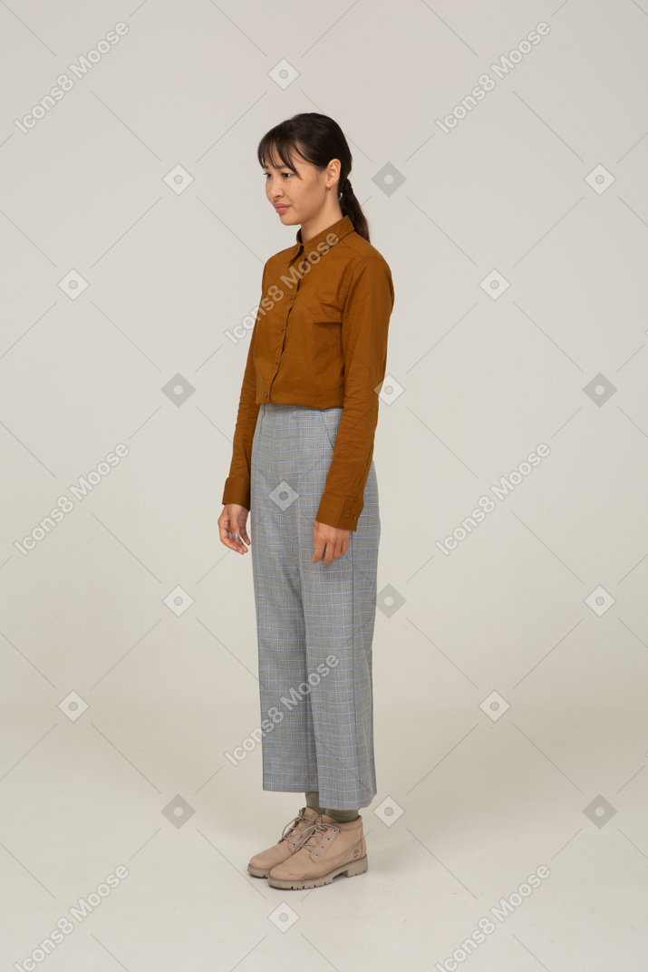 Vista di tre quarti di una giovane donna asiatica in calzoni e camicetta in piedi ancora