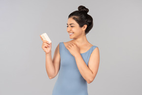 Young indian woman looking at cream bottle she's holding