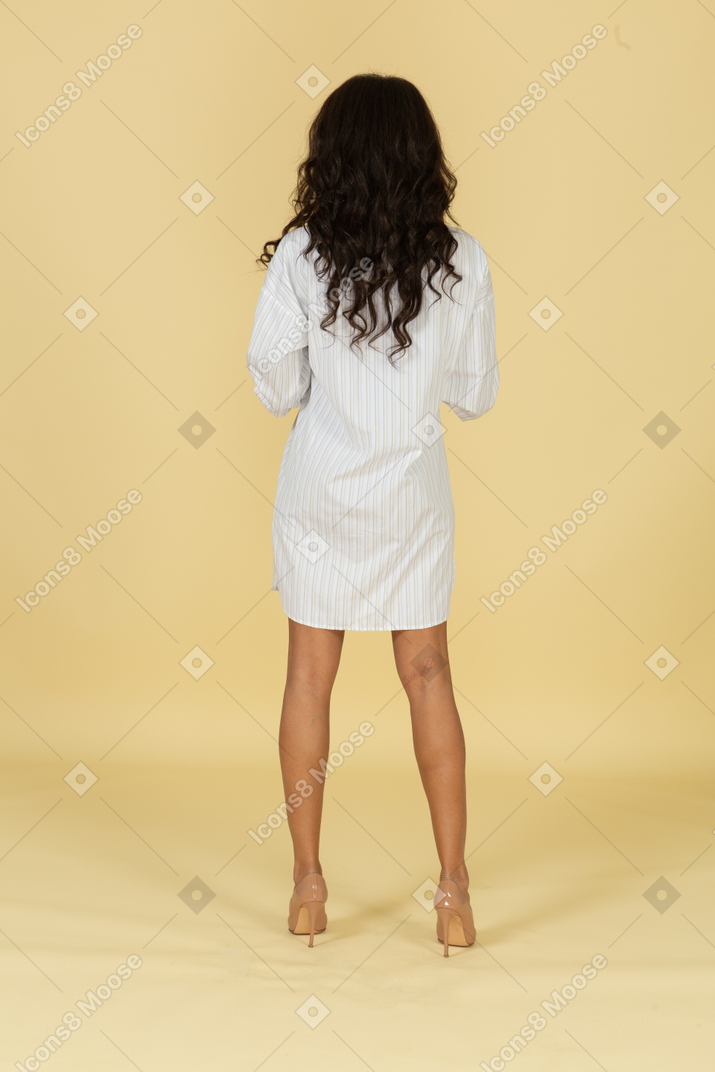 Back view of a dark-skinned young female buttoning up her white dress