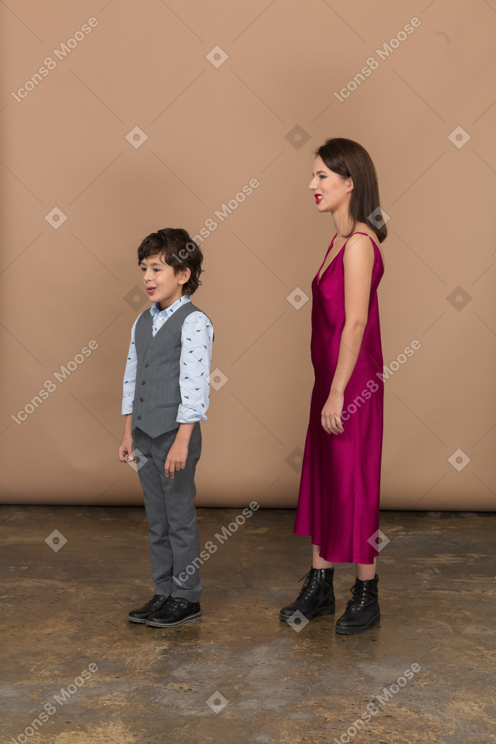 赤いドレスを着たうんざりした女性と横顔に立っている男の子