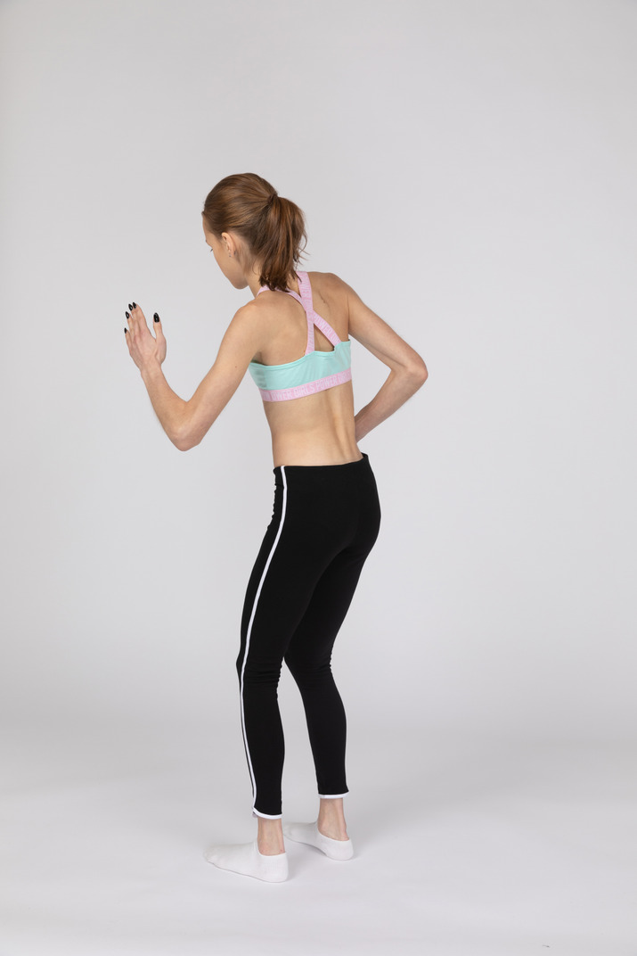 Three-quarter back view of a teen girl in sportswear leaning forward while standing like a robot