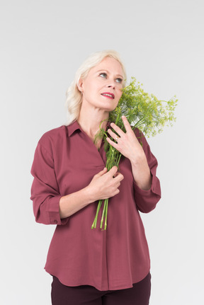 부르고뉴 셔츠를 입은 멋진 중년 금발 여성과 그녀의 손에 간단한 꽃 꽃다발