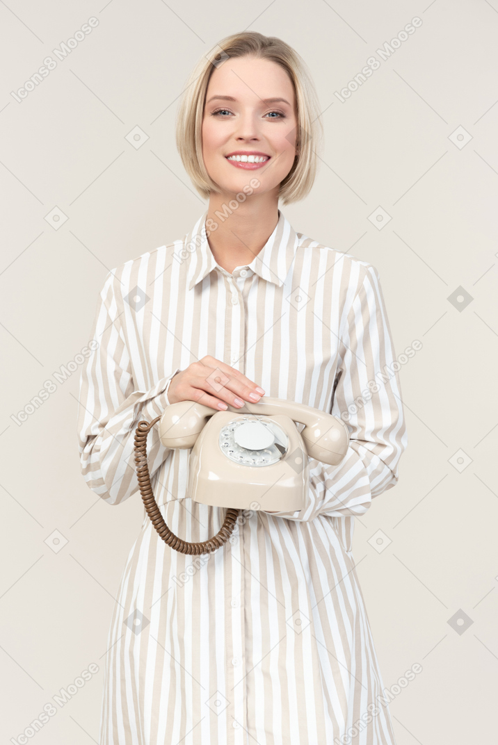 Улыбающаяся молодая женщина, держащая старый телефон