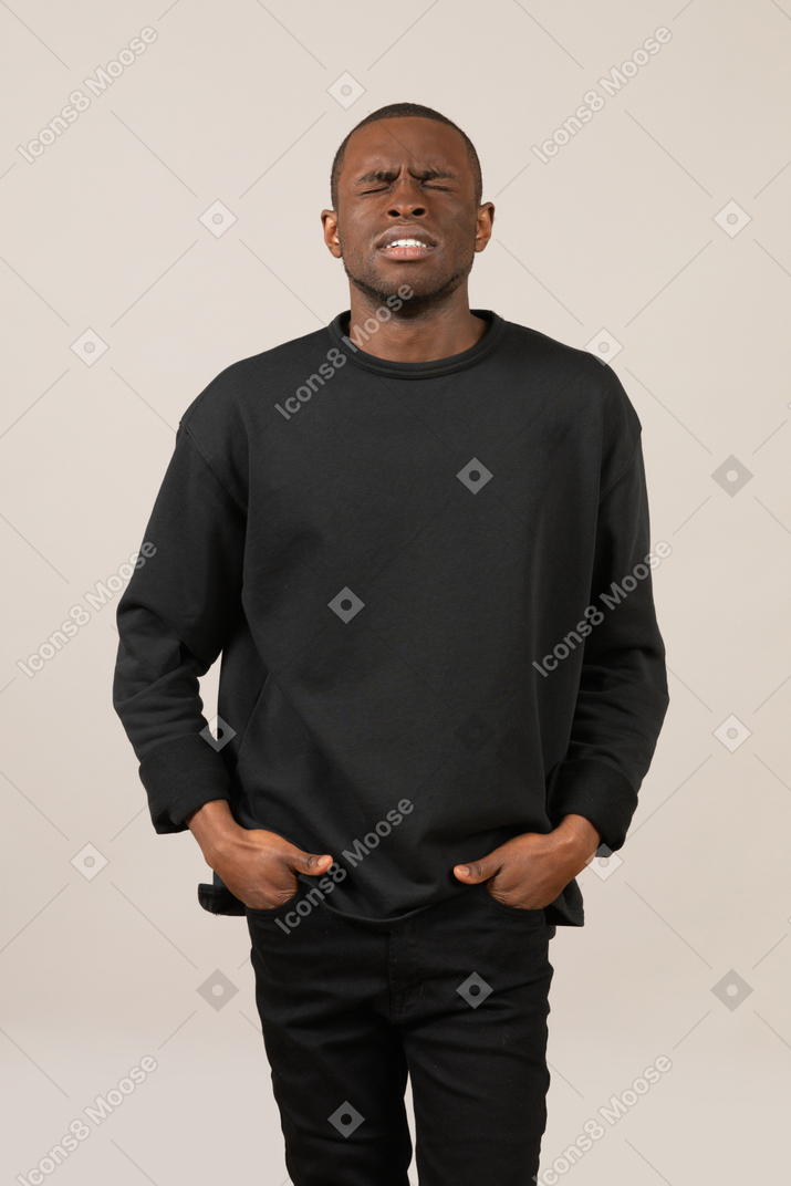 Young man with hands in pockets squeezing eyes