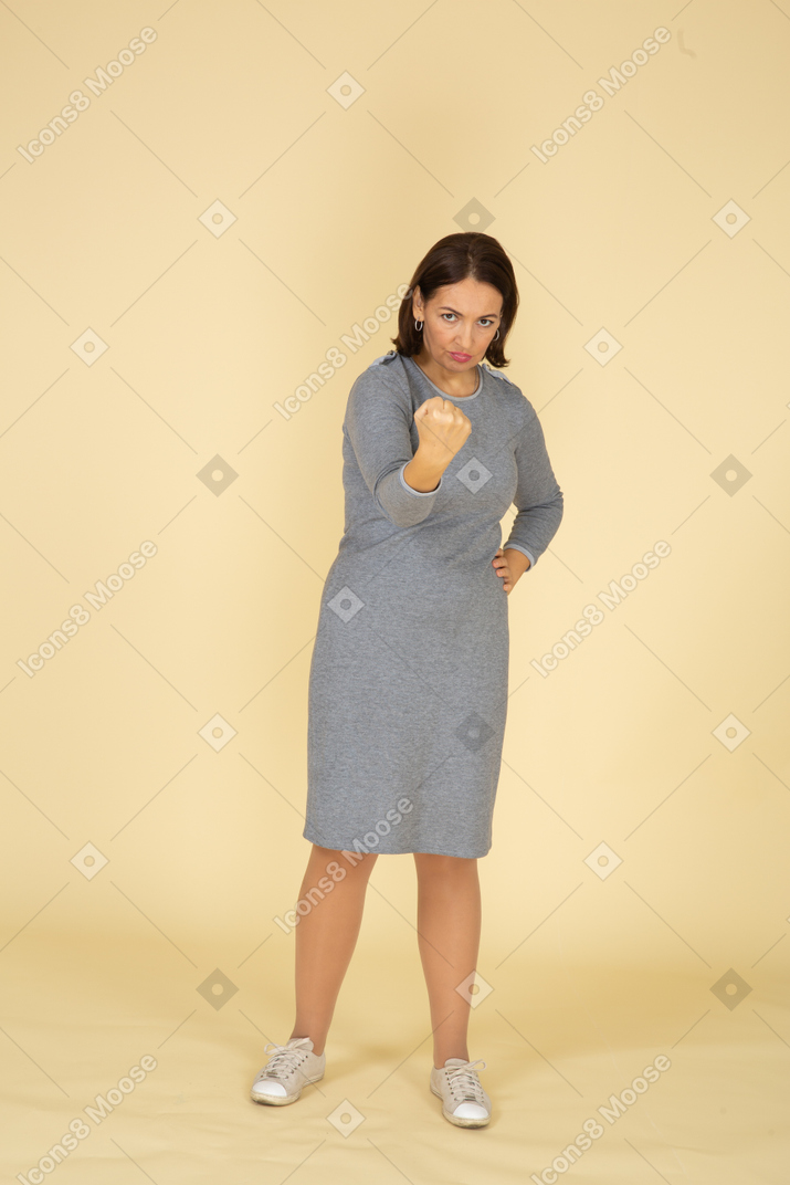 Front view of a woman in grey dress threatening someone with fist
