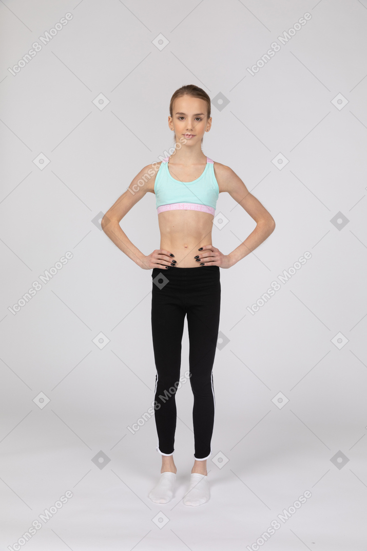 Vista frontal de uma adolescente em roupas esportivas colocando as mãos nos quadris