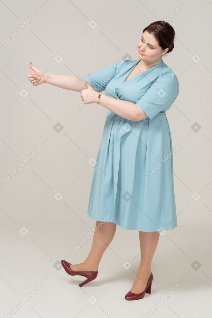 Вид спереди женщины в синем платье показывает палец вверх