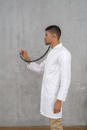 Vista lateral de un médico varón usando un estetoscopio