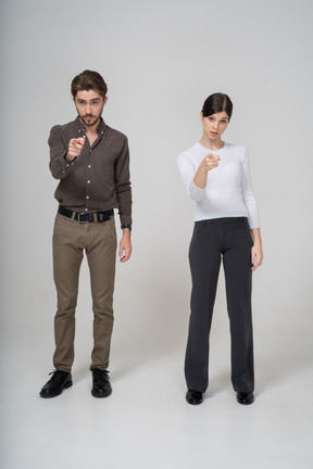 Front view of a young couple in office clothing pointing finger forward
