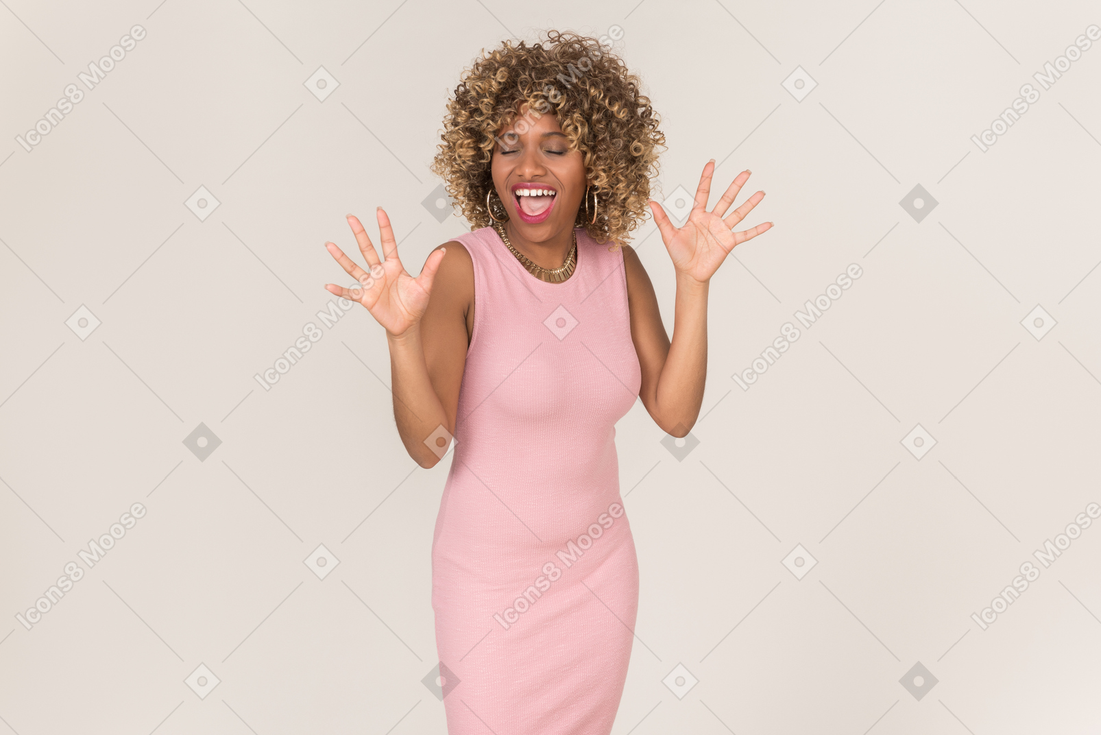A young black fluffy-haired woman in a pastel pink cocktail dress, having fun alone against a plain grey background