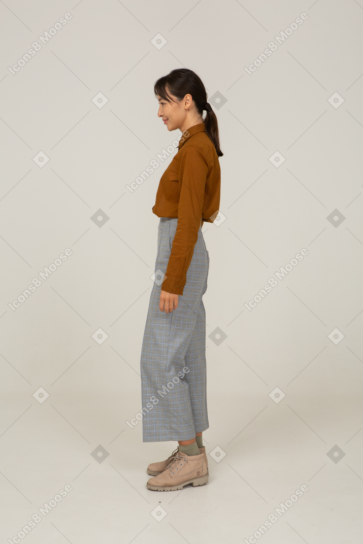Вид сбоку улыбающейся молодой азиатской женщины в бриджах и блузке