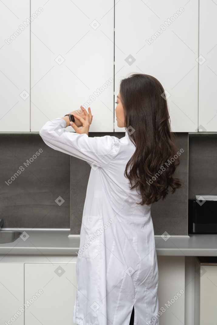 Woman in white lab coat standing and looking at her watch