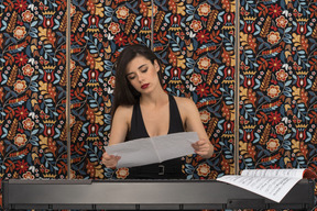 Confident female pianist looking at musical notation in hand while taking some notes