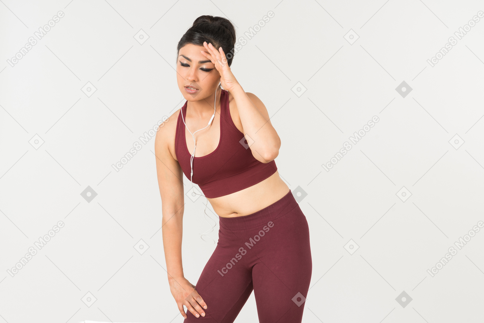 Tired looking young indian woman in sporstwear standing with headphones on her neck