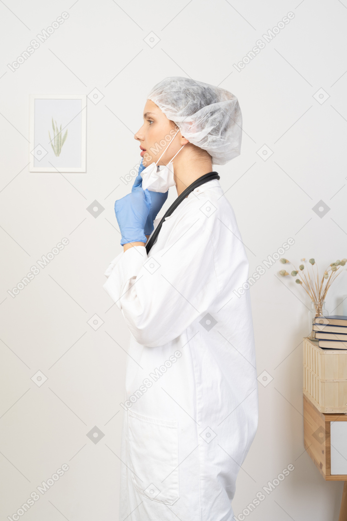 Vista lateral de una joven doctora poniéndose una máscara y mirando a un lado