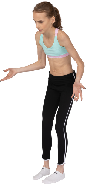 Three-quarter view of a teen girl in sportswear pointing hands somewhere down